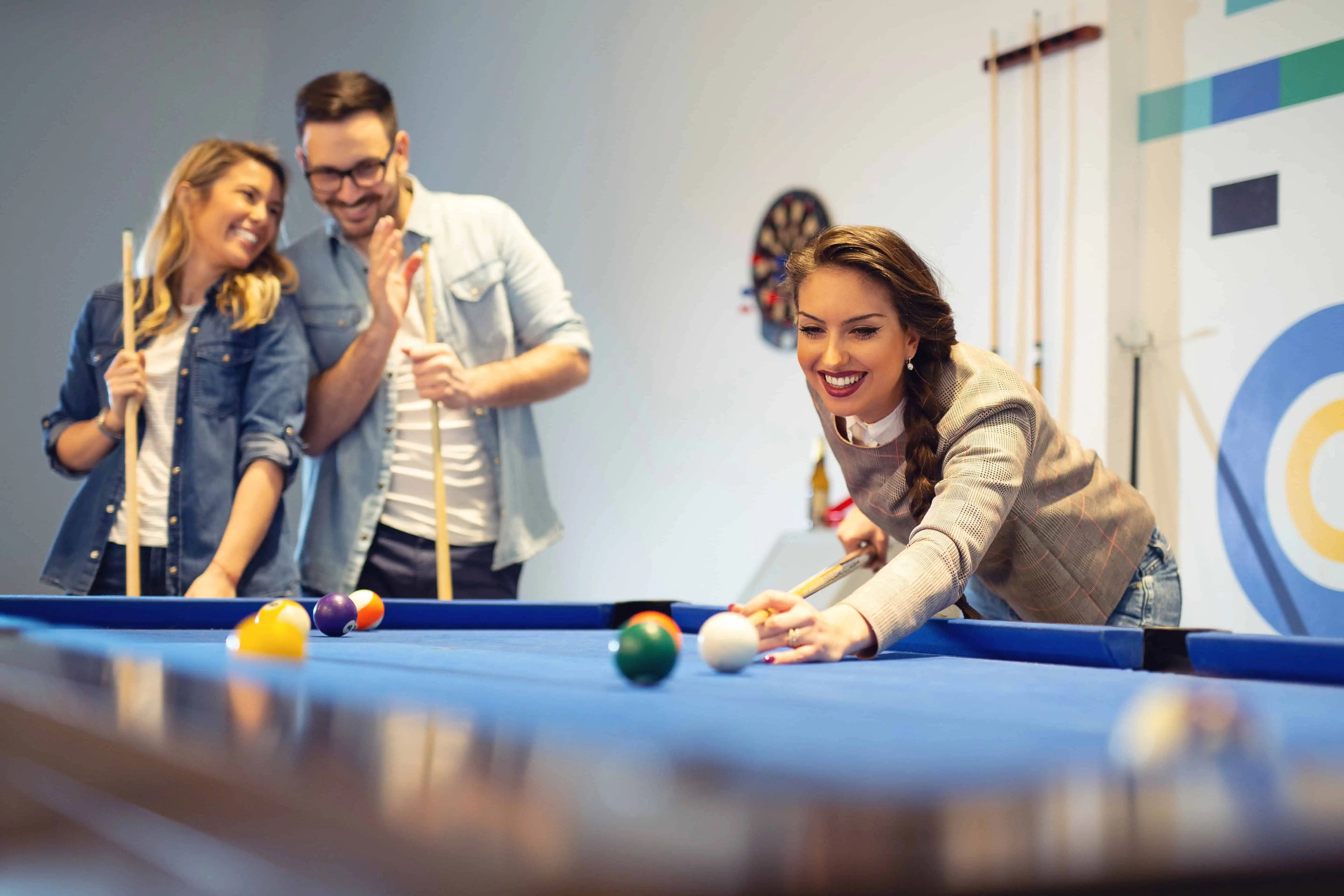 Friends laughing and playing pool around a modern billiards table